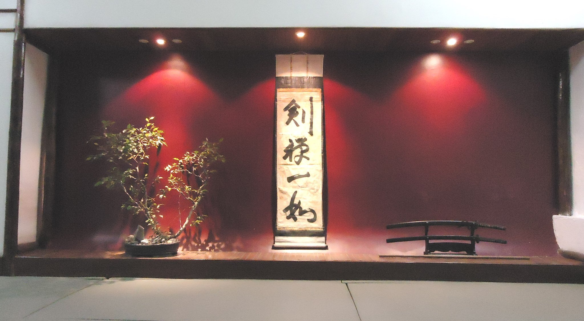 Tokonoma do dojo com pergaminho, bonsai e espadas